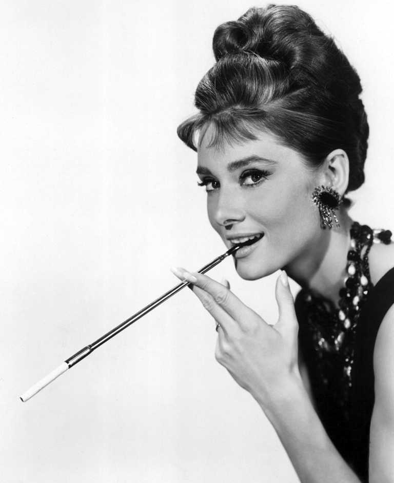 BRAH102 -4046329 Portrait noir et blanc iconique d'Audrey Hepburn dans Diamants sur canapé, posant avec élégance et tenant un long porte-cigarette.