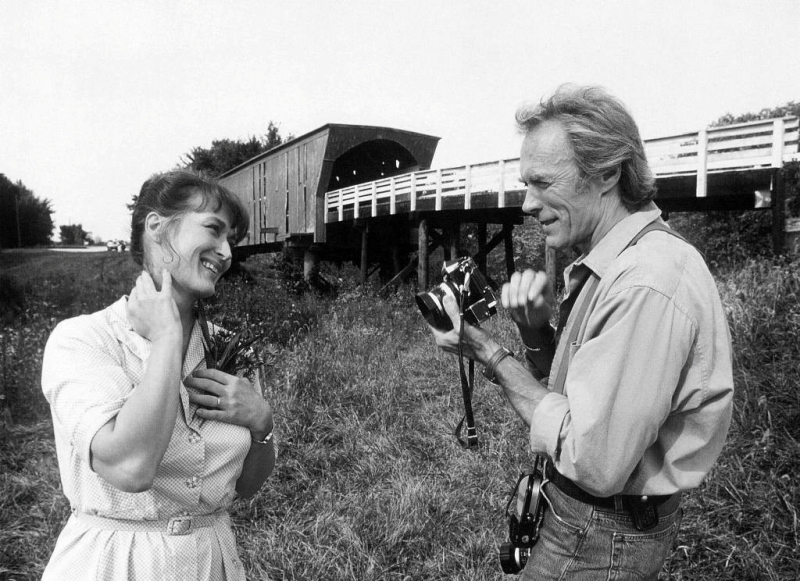 BRCL100NB - 1707408 Photographie noir et blanc de Clint Eastwood tenant un appareil photo face à Meryl Streep souriante, devant un pont couvert dans Sur la route de Madison.