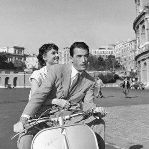 Photographie en noir et blanc d'Audrey Hepburn et Gregory Peck sur un scooter Vespa devant le Colisée à Rome, tirée du film Vacances Romaines.