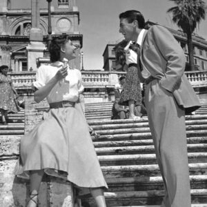 Photographie en noir et blanc d'Audrey Hepburn mangeant une glace sur les marches de la Place d'Espagne à Rome, face à Gregory Peck qui lui sourit.