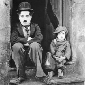 CC06 OK Photographie iconique en noir et blanc de Charlie Chaplin et du jeune acteur Jackie Coogan assis côte à côte sur un perron, dans leurs costumes fidèles au film Le Kid.