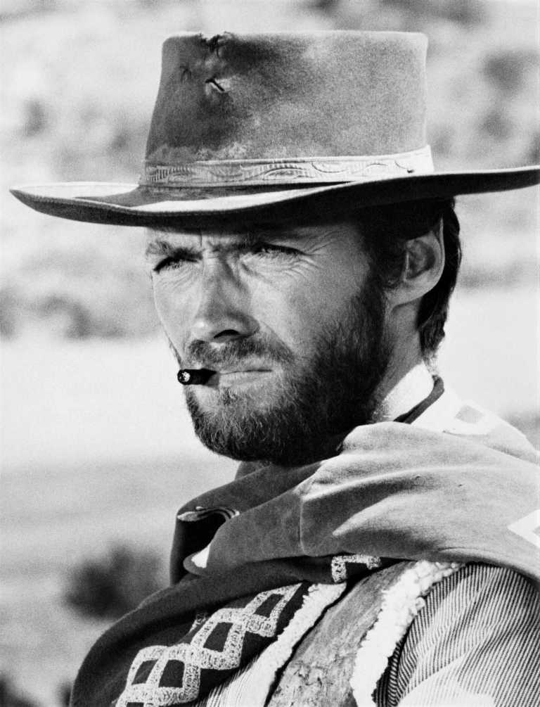 CL64 Affiche Eastwood Regard Acier : Gros plan en noir et blanc du visage de Clint Eastwood portant un chapeau de cowboy et un cigare aux lèvres, expression intense.