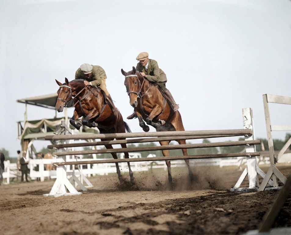 Duo de Saut (1925) : Affiche Équitation Vintage | Fuzars Photographie historique colorisée de 1925 montrant deux cavaliers et leurs chevaux franchissant simultanément un obstacle en bois lors d'un concours hippique.
