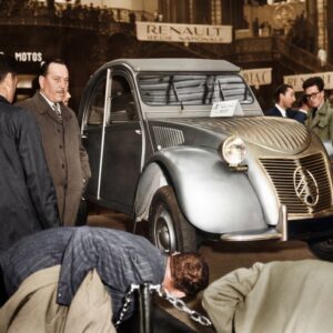 Photographie historique colorisée montrant la présentation de la première Citroën 2CV au Salon de l'Auto de Paris en 1948, entourée d'une foule de curieux.