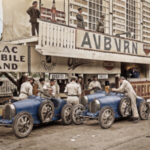 Bugatti au Grand Prix 1926 : Affiche Auto Vintage | Fuzars Photographie historique colorisée du Grand Prix d'Espagne 1926, montrant des mécaniciens préparant deux légendaires Bugatti bleues dans la voie des stands, sous des panneaux publicitaires d'époque.