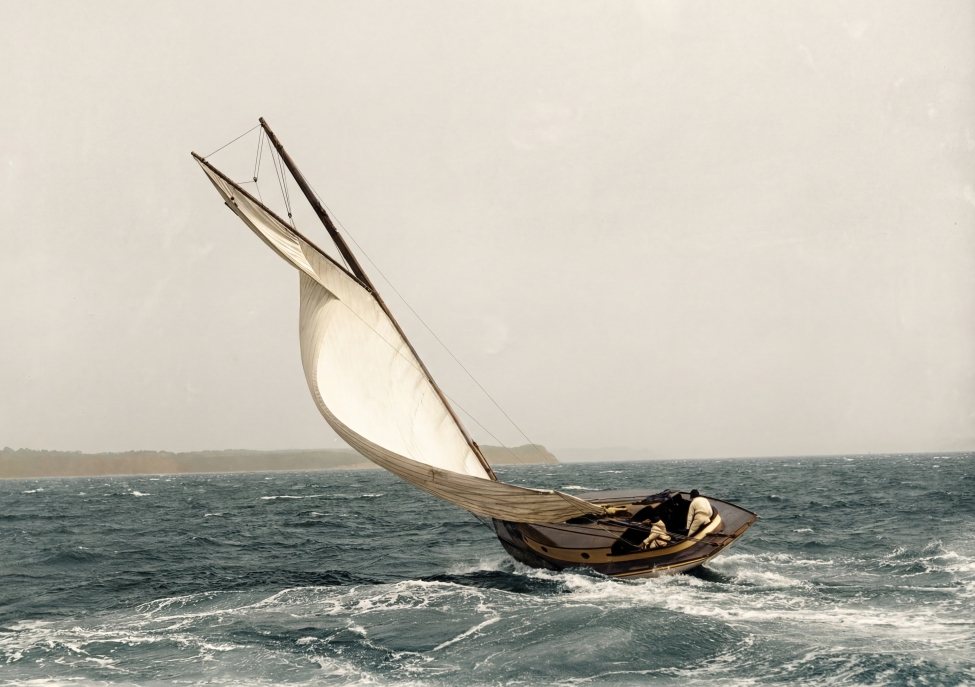 Affiche d'une photo historique colorisée de Fuzars montrant un voilier du début du 20ème siècle naviguant sur une mer agitée avec un équipage réduit.