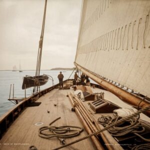 Photographie historique colorisée en vue subjective depuis le pont en bois du voilier Mayflower en 1886, montrant les cordages, l'immense voile et l'équipage.