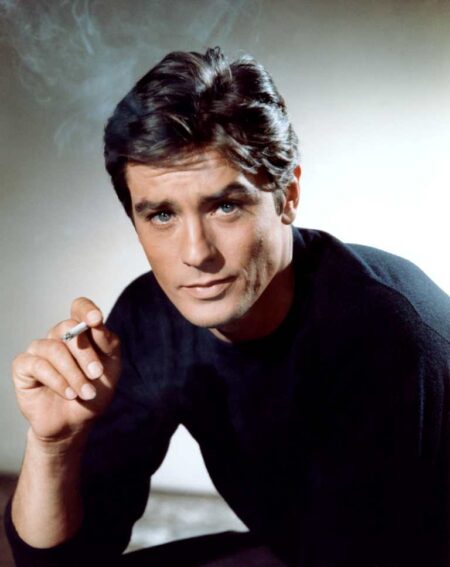 affiche couleur portrait d'Alain Delon dans le film Mélodie en sus soul, il porte un pull noir, regarde l'objetcif et tient une cigarette dans la main droite, il y a des volutes de fumée autour de lui