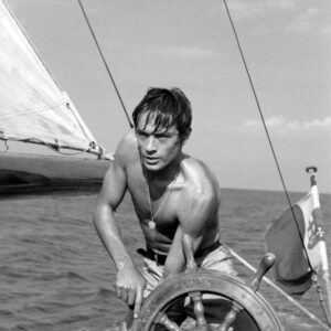 Affiche Delon Plein Soleil en noir et blanc : l'acteur Alain Delon torse nu manœuvre la barre d'un bateau en mer.