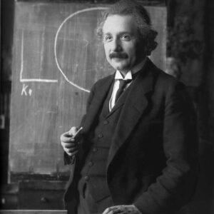 Albert Einstein : Le génie au tableau Photographie en noir et blanc d'Albert Einstein debout devant un tableau noir, tenant une craie à la main.