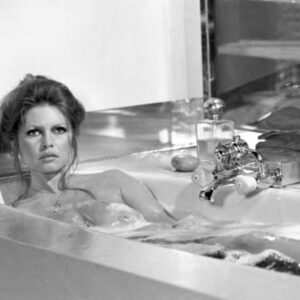 BRBB103NB - 4048703 Photographie en noir et blanc de Brigitte Bardot dans le film Don Juan 73, prenant un bain moussant. Elle regarde l'objectif avec une expression intense, les cheveux relevés, entourée de mousse avec un élégant flacon de parfum et des produits de bain posés sur le rebord de la baignoire en arrière-plan.