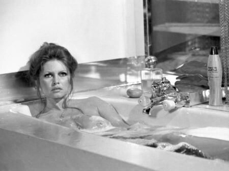 Photographie en noir et blanc de Brigitte Bardot dans le film Don Juan 73, prenant un bain moussant. Elle regarde l'objectif avec une expression intense, les cheveux relevés, entourée de mousse avec un élégant flacon de parfum et des produits de bain posés sur le rebord de la baignoire en arrière-plan.
