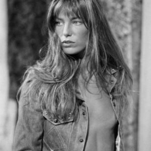 Photographie en noir et blanc de Jane Birkin avec sa célèbre frange, nue sous sa chemise en jean entrouverte.