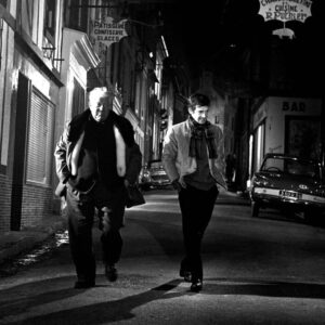 BRJG100 - 2025603 Plan large de nuit montrant Jean Gabin et Jean-Paul Belmondo marchant ensemble dans une rue vide éclairée par des enseignes dans le film Un Singe en Hiver.