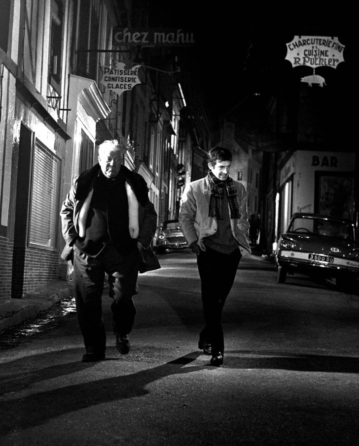 BRJG100 - 2025603 Plan large de nuit montrant Jean Gabin et Jean-Paul Belmondo marchant ensemble dans une rue vide éclairée par des enseignes dans le film Un Singe en Hiver.