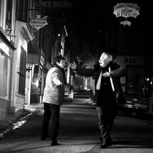 Jean Gabin les bras grands ouverts mimant un toreador face à Jean-Paul Belmondo dans une rue la nuit, scène joyeuse du film Un Singe en Hiver.