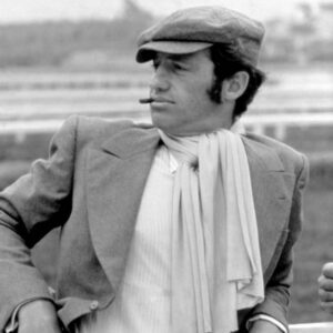 Affiche Belmondo Le Magnifique : Portrait noir et blanc de Jean-Paul Belmondo accoudé à une barrière, portant une casquette, une écharpe blanche et fumant un cigare