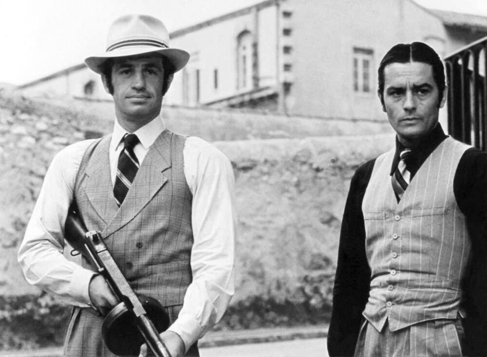 Affiche noir et blanc du film Borsalino montrant Jean-Paul Belmondo avec un chapeau et une mitraillette aux côtés d'Alain Delon en costume 3 pièces