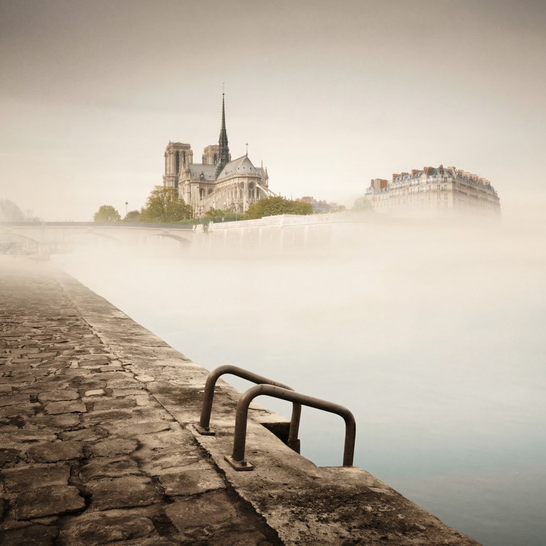 Vue artistique de la cathédrale Notre-Dame de Paris émergeant d'une brume épaisse au-dessus de la Seine. Photographie colorisée aux tons crème et sépia.