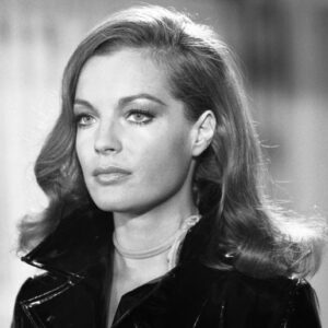 Photographie en noir et blanc de Romy Schneider dans le film Max et les Ferrailleurs, portant un manteau en vinyle brillant et un fin collier, regardant au loin avec une expression captivante.
