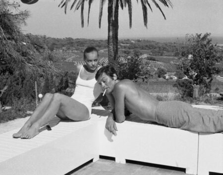 Photographie noir et blanc vintage d'Alain Delon et Romy Schneider en maillot de bain discutant au bord d'une piscine, ambiance film La Piscine 1969.