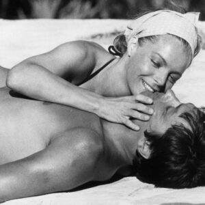 Photographie de cinéma en noir et blanc montrant Alain Delon et Romy Schneider allongés l'un contre l'autre dans une scène intime du film La Piscine.