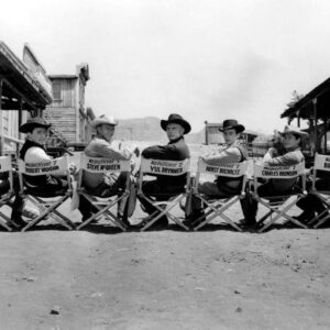 Photo panoramique noir et blanc du casting du film Les Sept Mercenaires assis sur des chaises de réalisateur : Steve McQueen, Yul Brynner, Charles Bronson et les autres acteurs en tenues de cowboys.