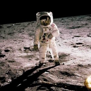 Premier Pas : L'Homme sur la Lune (Apollo 11) Photographie historique haute définition d'un astronaute de la NASA debout sur la surface de la Lune, tenant un instrument scientifique. Le module lunaire LEM et le drapeau américain sont reflétés dans sa visière dorée.