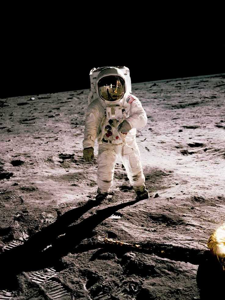 Premier Pas : L'Homme sur la Lune (Apollo 11) Photographie historique haute définition d'un astronaute de la NASA debout sur la surface de la Lune, tenant un instrument scientifique. Le module lunaire LEM et le drapeau américain sont reflétés dans sa visière dorée.
