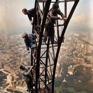 Photographie historique colorisée des ouvriers peintres travaillant sur la structure en fer de la Tour Eiffel, surplombant le Champ-de-Mars et Paris.