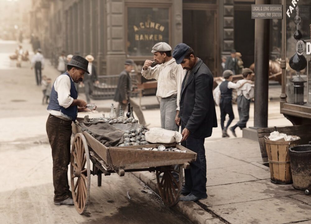 Photographie historique colorisée de 1930 montrant trois hommes tenant un étal de rue proposant des clovisses fraîches ('CLAMS') dans une ville américaine. Le panneau indique 'OPEN AT ALL TIMES - CLAMS - 20c doz'. Architecture en briques et voitures d'époque en arrière-plan.