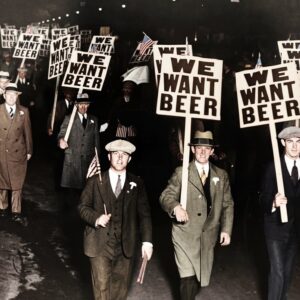 Manifestation We Want Beer : Affiche Vintage & Humour | Fuzars Photographie historique colorisée montrant une foule d'hommes en costume manifestant la nuit contre la Prohibition aux États-Unis, brandissant des panneaux "WE WANT BEER".