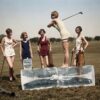 Photographie historique colorisée montrant cinq jeunes femmes en maillots de bain vintage sur un golf. L'une d'elles prépare son swing debout sur d'énormes blocs de glace.