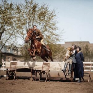 Affiche Cheval Saut Vintage : photographie d’art colorisée vers 1930 montrant un cavalier et son cheval sautant au-dessus d'une table dressée où sont assises deux femmes avec un chien Collie, lors d'une démonstration équestre.