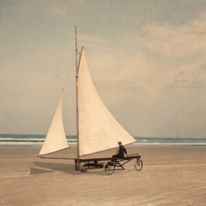 BDM25COU Affiche Char Voile Vintage : photographie du début du XXe siècle montrant un pionnier en uniforme sur un char à voile primitif sur une immense plage déserte.