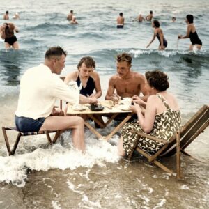 Affiche Pique-Nique Mer Vintage : photographie des années 30 montrant quatre personnes attablées dans l'eau de mer, prenant le thé ou le café au milieu des vagues sur une plage animée.