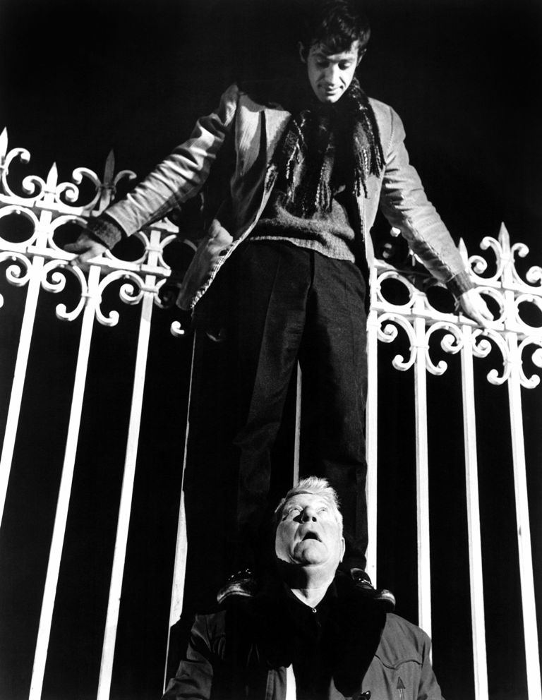 BRJG114 - 1781176 Affiche Singe en Hiver : photographie en noir et blanc de 1962 montrant Jean-Paul Belmondo debout sur les épaules de Jean Gabin, escaladant une imposante grille en fer forgé la nuit.
