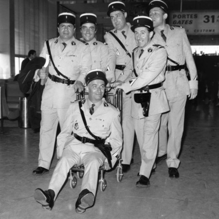 Affiche Gendarmes St Tropez : photographie d'art en noir et blanc de 1965 montrant Louis de Funès assis sur un chariot à bagages entouré de sa brigade à l'aéroport.