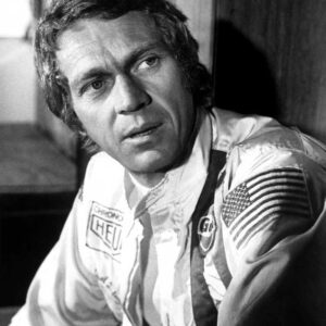Affiche Pilote Steve McQueen : portrait en noir et blanc de Steve McQueen en tenue de course officielle, portant les logos Gulf et Heuer, capturé en 1971 sur le circuit de la Sarthe.