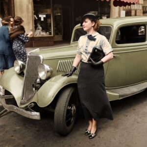 MOD22COU Affiche Mode Automobile Vintage Élégance : photographie d'art colorisée vers 1935 montrant une femme élégante en chapeau et gants posant à côté d'une Ford V8 verte des années 1930 dans une rue urbaine avec un auvent rouge.