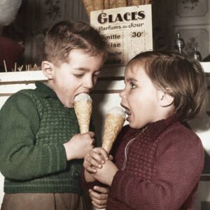Affiche Enfants Glace Paris 1954 : photographie d'art colorisée montrant deux jeunes enfants en pulls de laine dégustant avec gourmandise un cornet de glace devant une échoppe parisienne en 1954.