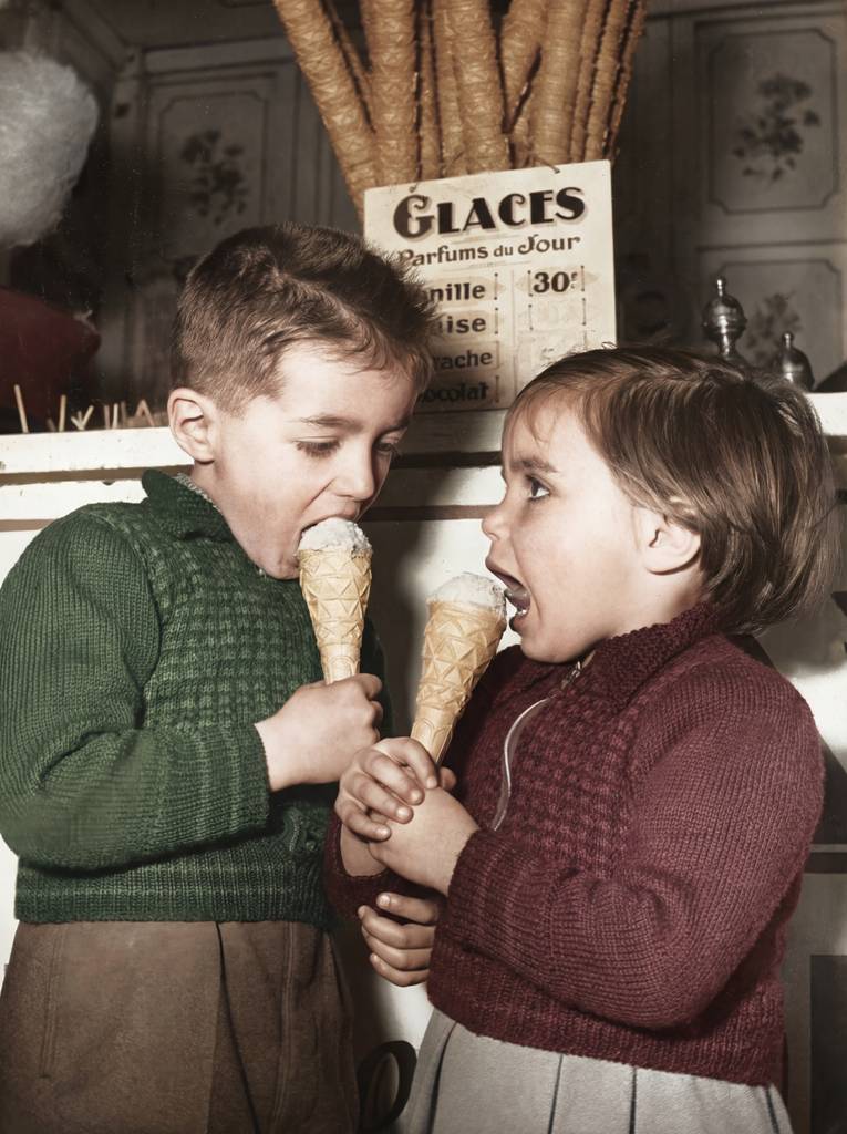 PAR74COU Affiche Enfants Glace Paris 1954 : photographie d'art colorisée montrant deux jeunes enfants en pulls de laine dégustant avec gourmandise un cornet de glace devant une échoppe parisienne en 1954.