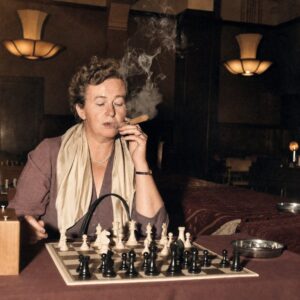 Affiche Ingrid Larsen Échecs : photographie d’art colorisée de 1954 montrant la championne danoise Ingrid Larsen en pleine concentration lors d'un tournoi à Amsterdam, un cigare à la main avec d'épaisses volutes de fumée s'élevant au-dessus de l'échiquier.