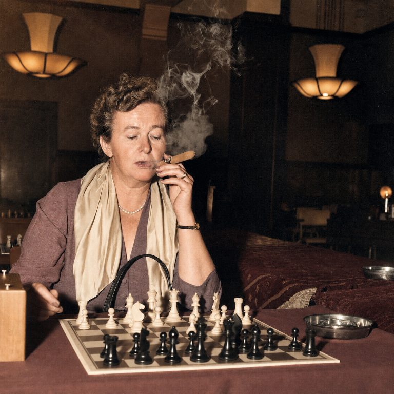 Ingrid Larsen aux échecs Affiche Ingrid Larsen Échecs : photographie d’art colorisée de 1954 montrant la championne danoise Ingrid Larsen en pleine concentration lors d'un tournoi à Amsterdam, un cigare à la main avec d'épaisses volutes de fumée s'élevant au-dessus de l'échiquier.