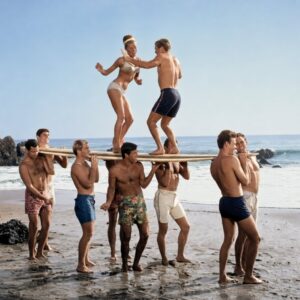 image.png Affiche Surf Vintage Plage : photographie d'art des années 60 montrant un groupe de jeunes surfeurs portant une planche sur leurs épaules, avec un couple dansant en équilibre au-dessus d'eux sur le sable.