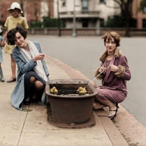 Photographie vintage colorisée de 1927 montrant deux jeunes femmes élégantes s'amusant à une pêche aux canards de rue devant des enfants.
